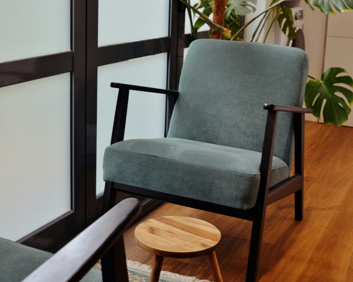 A green armchair by a frosted window in the office, a plant behind it