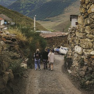 Travelers walking a stone-walled path into a mountain village