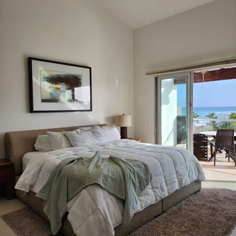 A bright room with white linen and doors open onto a sea-view terrace