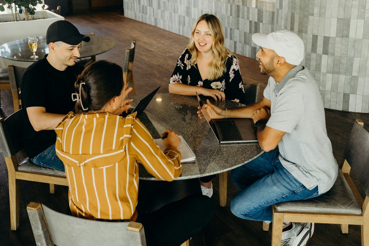 Four colleagues talking around a table with laptops open