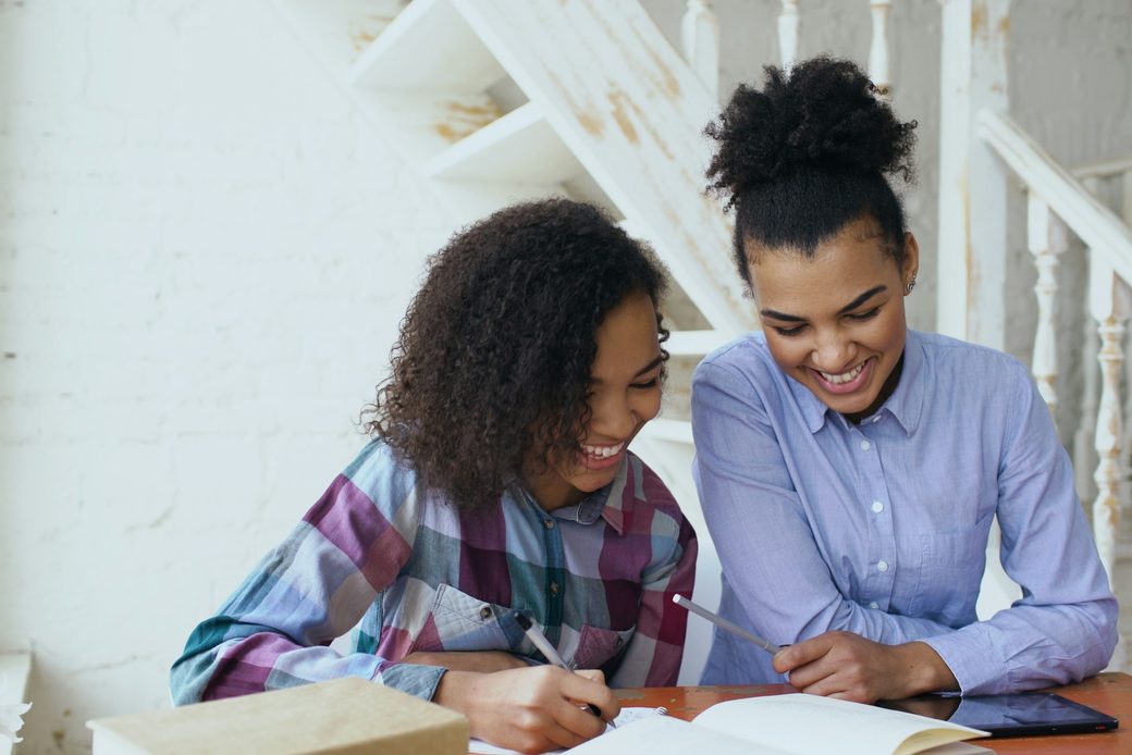 A tutor and a student smiling over an open notebook at a table