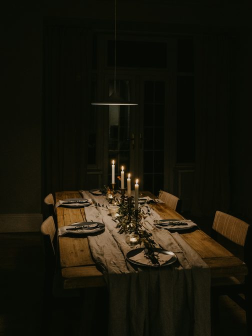 A long candlelit table set for dinner in a dark room