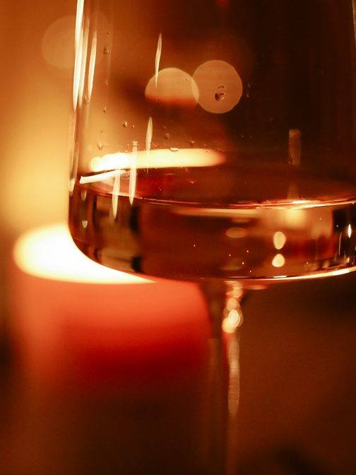 A glass of wine glowing in front of a candle