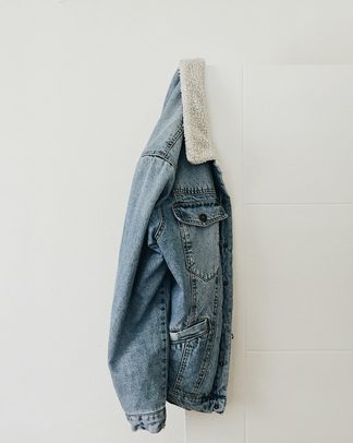A washed denim jacket with a fleece collar hanging on a white wall