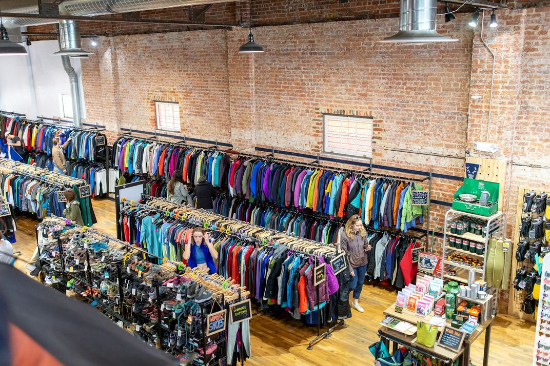 Racks of colorful vintage clothing in a bright, brick-walled shop