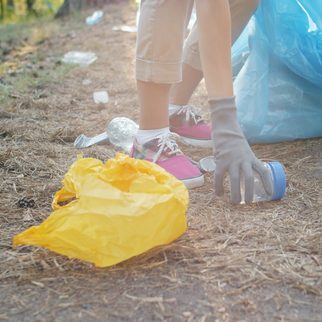 A volunteer in gloves picking up litter into a blue bag