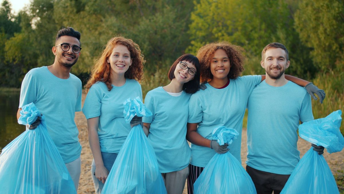 A group of smiling volunteers holding full trash bags in a park