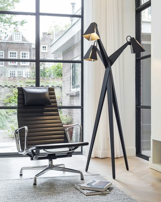 A black floor lamp beside a lounge chair by a tall window