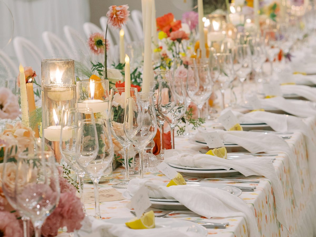 A long wedding table set with candles, glassware and pink flowers