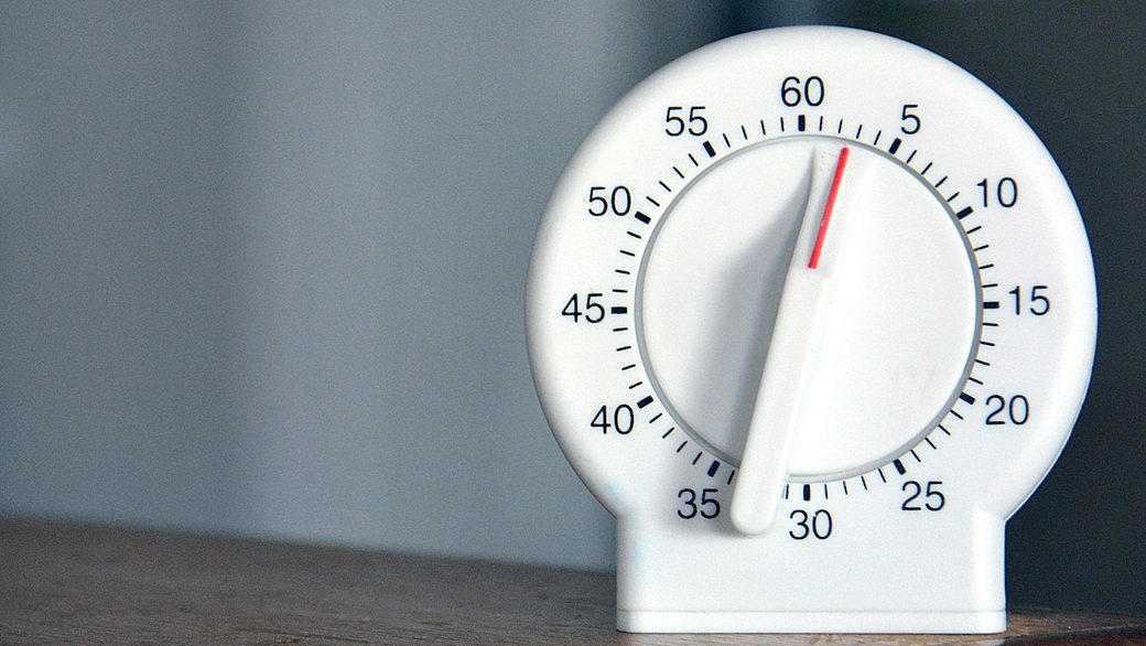 A white wind-up timer on a wooden shelf