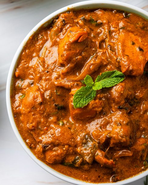 A bowl of tomato curry topped with a sprig of mint