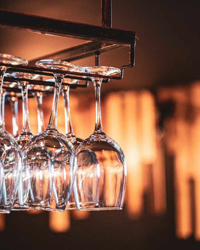 Wine glasses hanging upside down from a rack in warm bar light