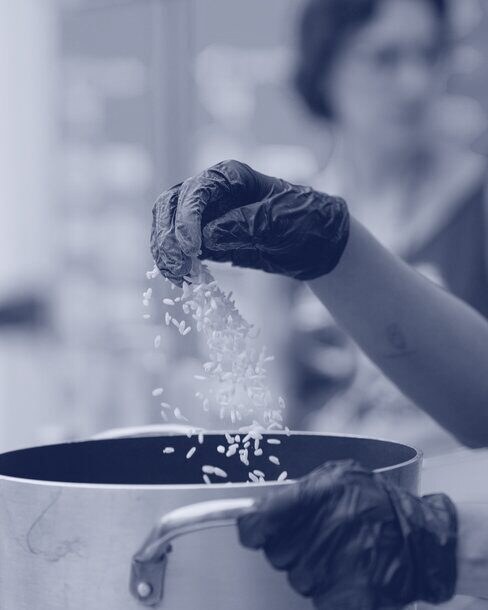 A volunteer's gloved hand pouring rice into a pot