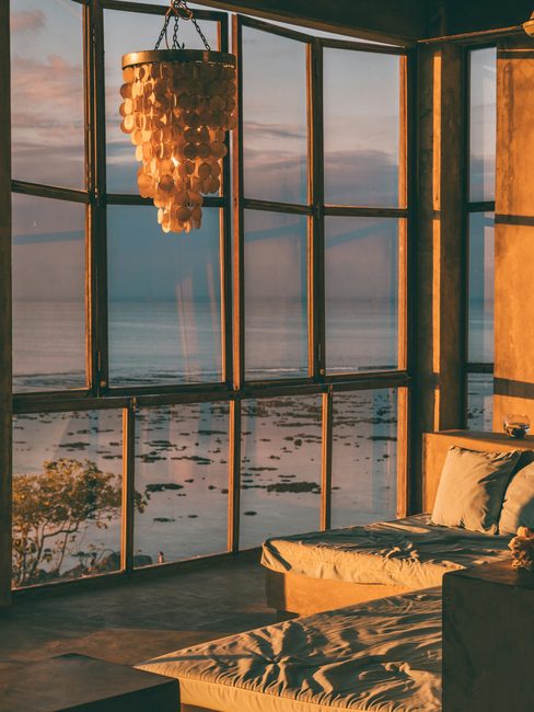 A quiet bedroom with tall windows onto the sea at sunset