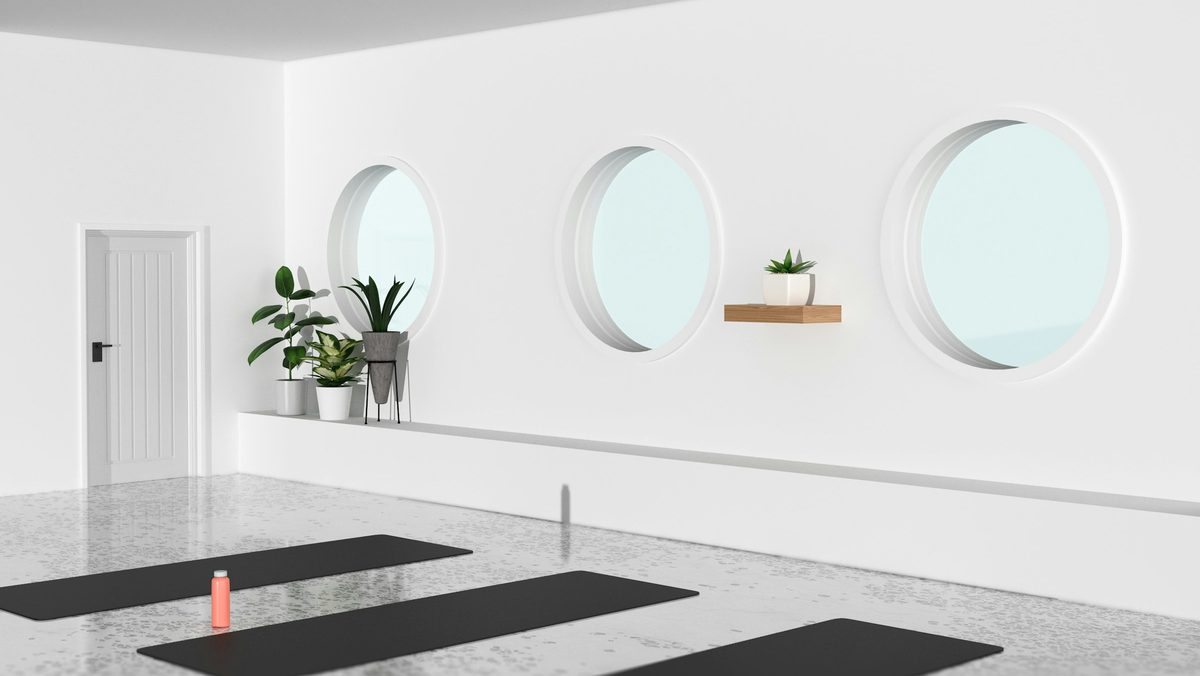 A bright white studio with three round windows and mats laid out on the floor